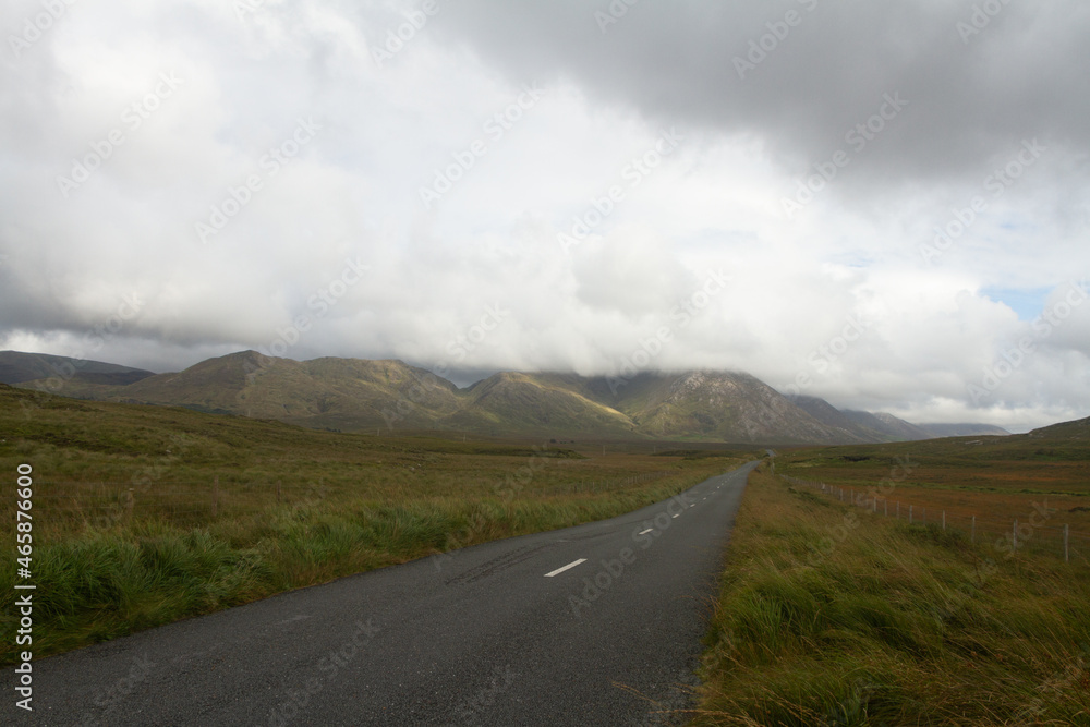 Empty road leading through Connemara National Park mountains under cloud selective focus