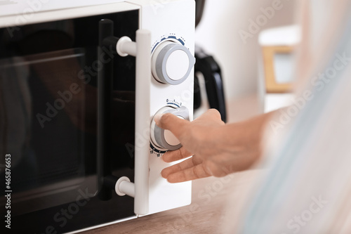 Young woman adjusting microwave oven in kitchen, closeup