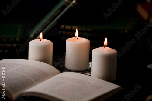 candles with flame, and reading book on desk, black background. (focus on candle).