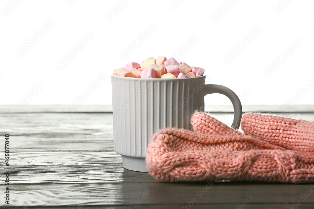 Cup of cocoa with marshmallows and gloves on table against white background Cup of cocoa with marshmallows and gloves on table against white background