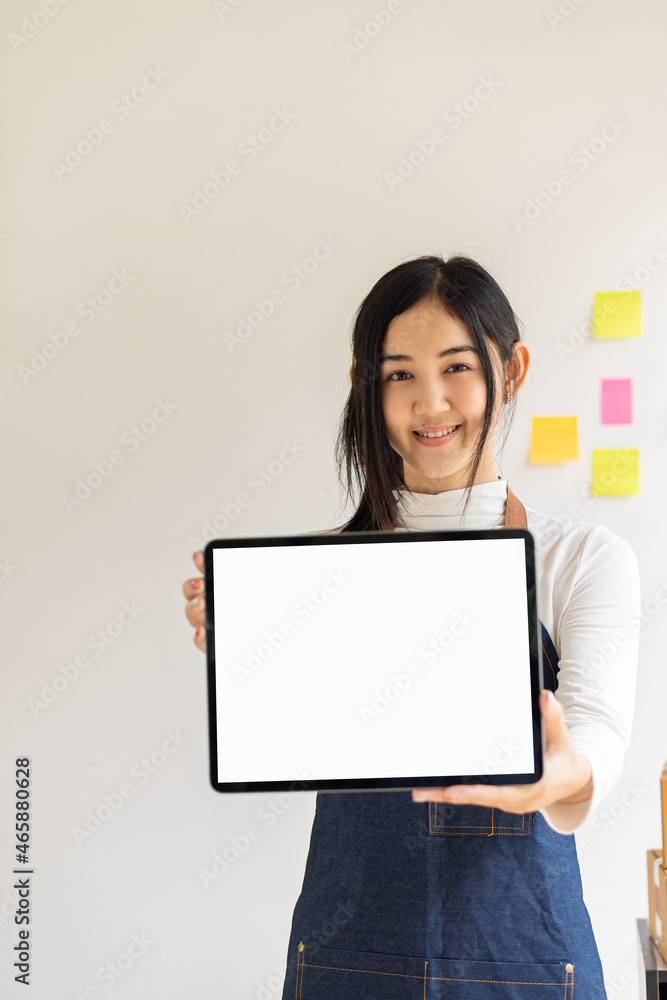 Beautiful Asian woman holding and showing white tablet with a blank screen in the modern coffee shop against white wall background. Beautiful Asian woman holding and showing white tablet with a blank screen in the modern coffee shop against white wall background.