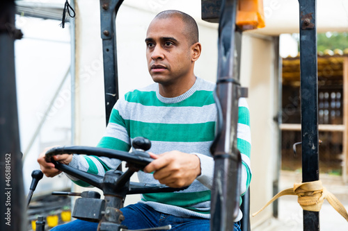 Skilled hispanic worker of materials warehouse working on forklift truck