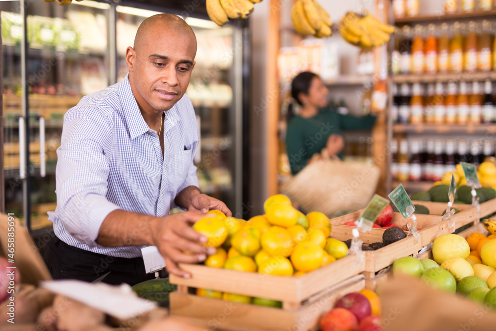 Male consumer choosing ripe tangerines in supermarket