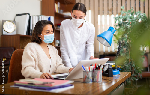 Confident female executive with assistant wearing protective face masks for disease protection working with papers in office