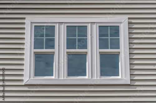 Triple hung window with fixed top sash and bottom sash that slides up  sash divided by white grilles a surrounded by white elegant frame  horizontal white vinyl siding on a new construction residence