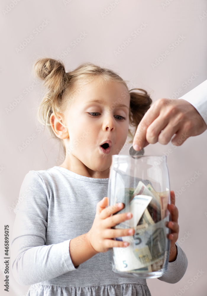 Surprised emotional child girl isolated background holds jar with banknotes.Excited expression face.Kid save money and account banking for finance concept. Father businessman put coin to bank Surprised emotional child girl isolated background holds jar with banknotes.Excited expression face.Kid save money and account banking for finance concept. Father businessman put coin to bank