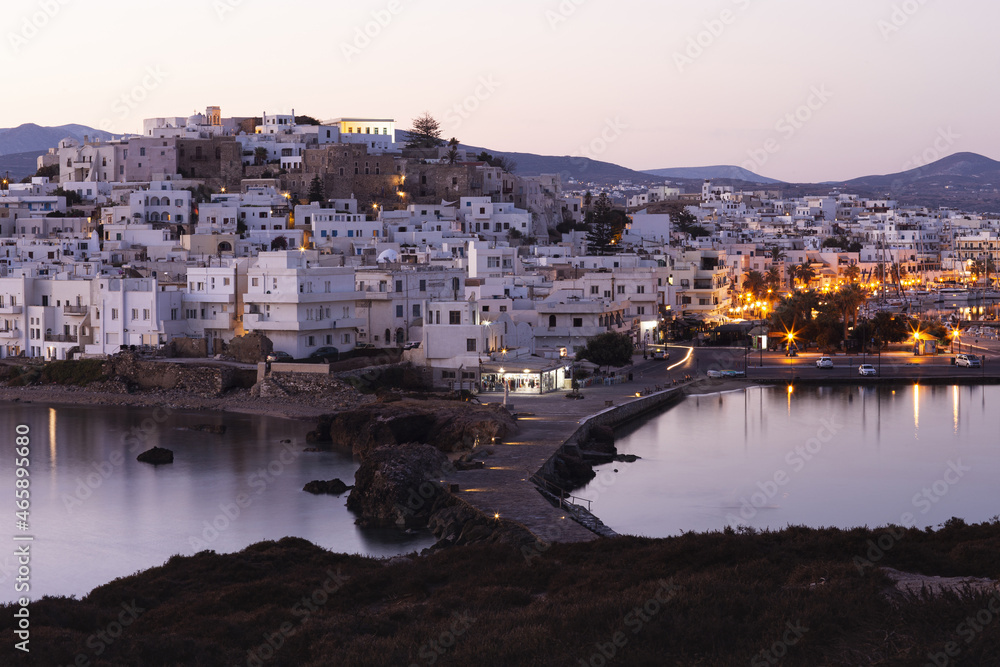 Pink morning over a mountainous Greek island with a white city. Street lights are reflected in the calm sea