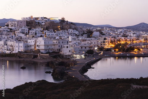 Pink morning over a mountainous Greek island with a white city. Street lights are reflected in the calm sea © Elena