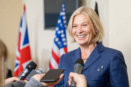 Photo Smiling mature female politician with blond hair talking to press after summit w