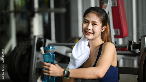 Young fitness woman with towel taking a break and drinking water after workout.