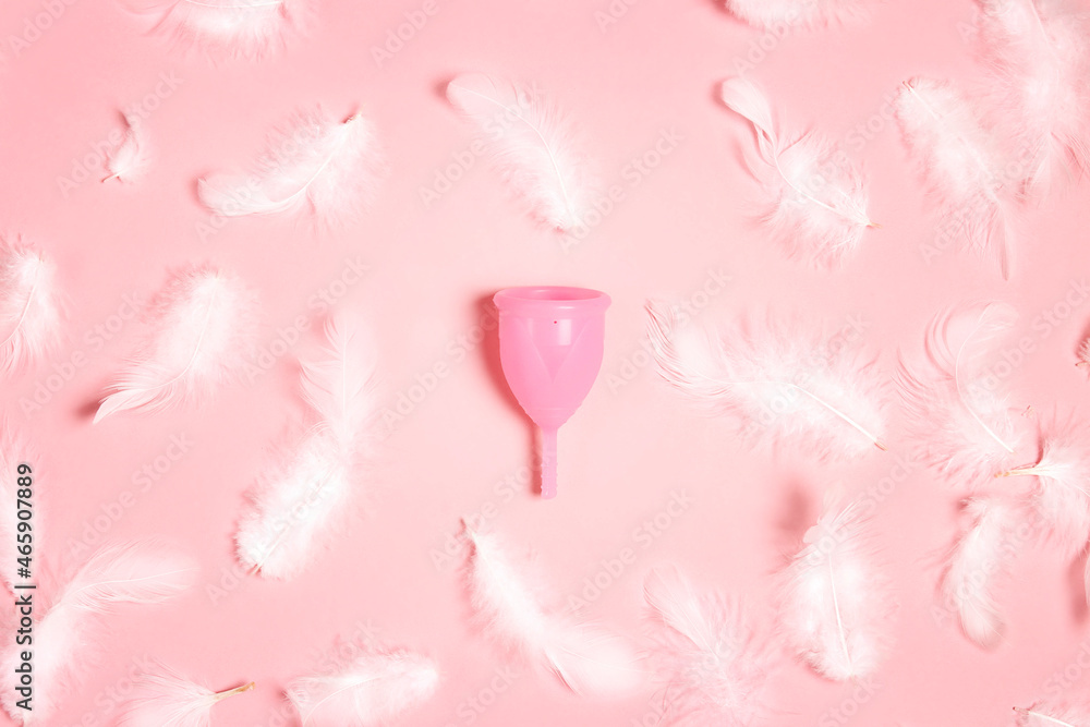 Menstrual cup surrounded by white feathers on a pink background. Menstrual cup surrounded by white feathers on a pink background.