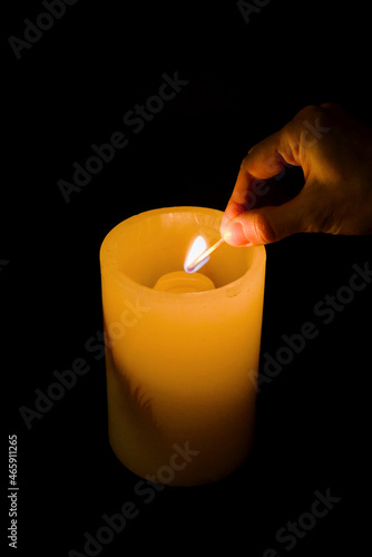 Burning candle with a hand with a matchstick, dark background, copy space