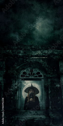 Halloween witch holding black face mask standing over ancient castle window, full moon with spooky cloudy sky, Halloween mystery concept