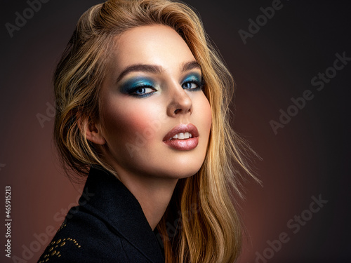 Portrait of sexy blonde woman with a beautiful face. Fashion model with long hair, studio shot.  Photo of young stylish  woman in black clothes with  blue make-up.