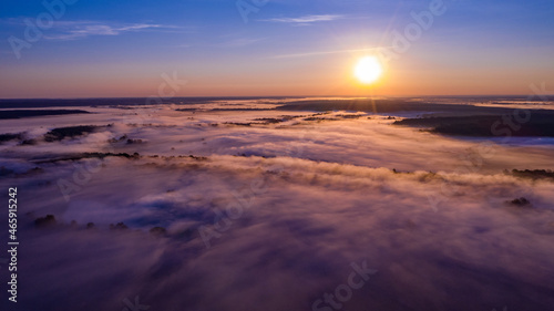 Aerial  view of a beautiful summer  landscape with a fog while dawn.  Photo from drone of a foggy landscape in spring. Top view to land while sunrise. Sun is above the horizon © Valua Vitaly