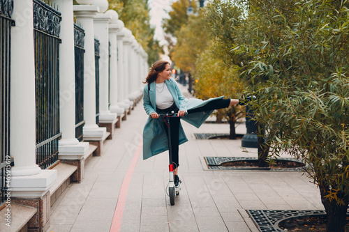 Fototapeta Young woman riding electric scooter in autumn city