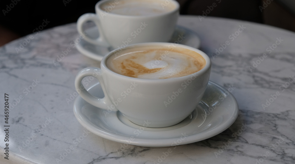 Two cups of cappuccino or latte decorated with foam on marble table background in Coffee shop. Morning coffee for couple in love. Close-up. Two white mugs of coffee.