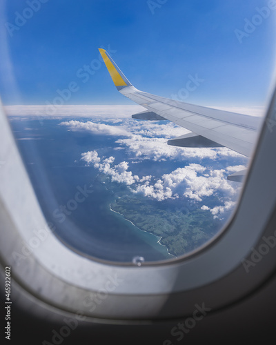 Vue d'un hublot sur l'aile de l'avion, au dessus de la mer ou de l'océan bleu avec des nuages. 