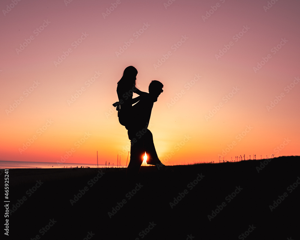 Couple en silhouette, amoureux. Un couché de soleil derrière le couple, elle est portée par son petit ami.