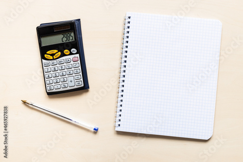 top view of blank sheet of squared paper of spiral notebook, pen and financial calculator on light brown wooden board photo