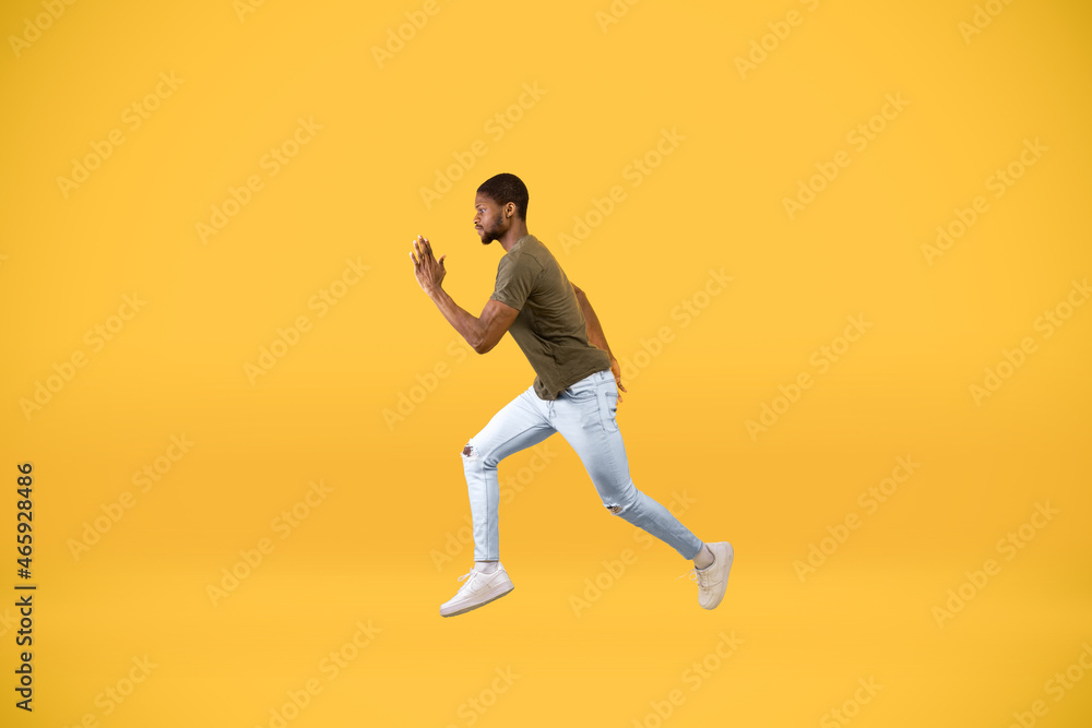 Young african american man running over yellow studio background, in motion side view shot of guy jumping in air