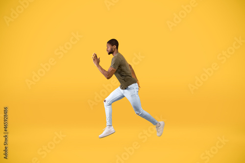 Young african american man running over yellow studio background  in motion side view shot of guy jumping in air