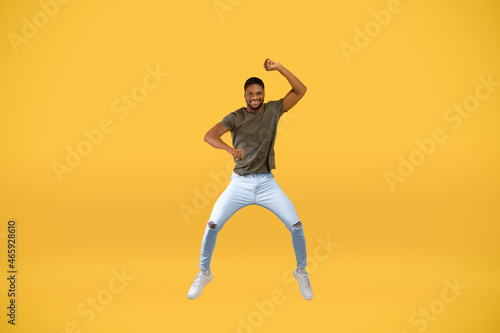 Expressing joy. Full length studio shot of active black man jumping over yellow background, free space