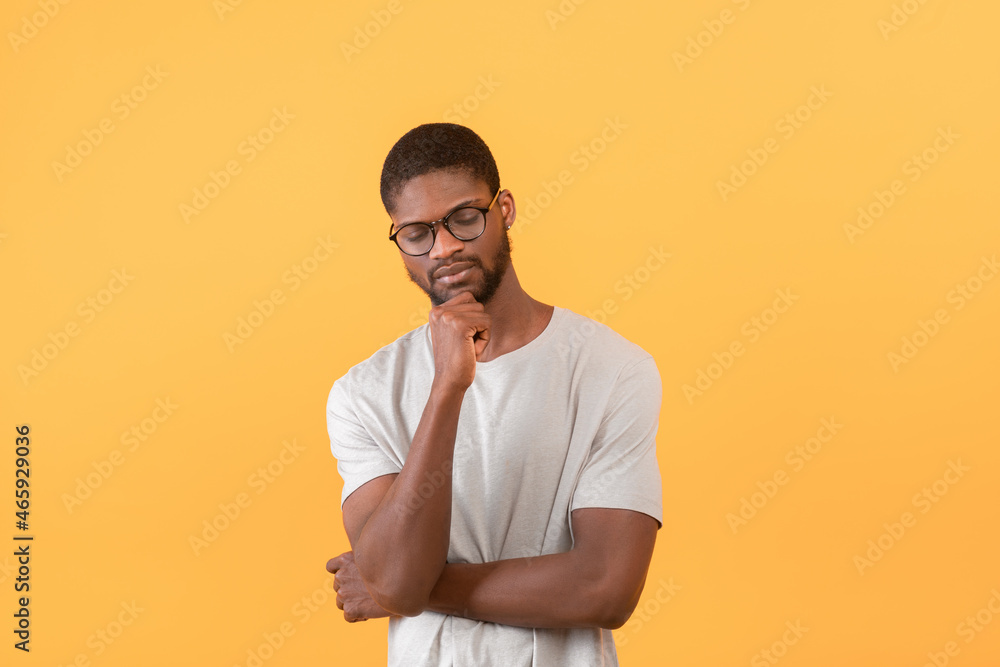 Thoughtful african american guy touching chin and thinking about something, standing over yellow background Thoughtful african american guy touching chin and thinking about something, standing over yellow background
