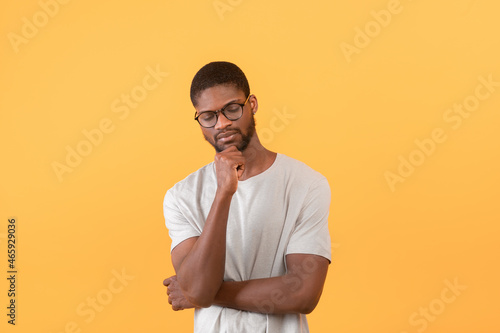 Thoughtful african american guy touching chin and thinking about something, standing over yellow background