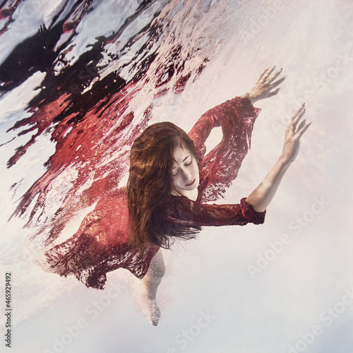 A girl in a red lace dress swims underwater as if flying on a light background