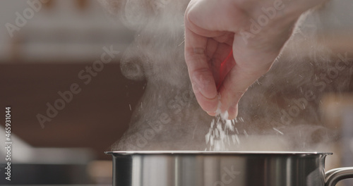 Fotografie man adding salt to boiling water in saucepan