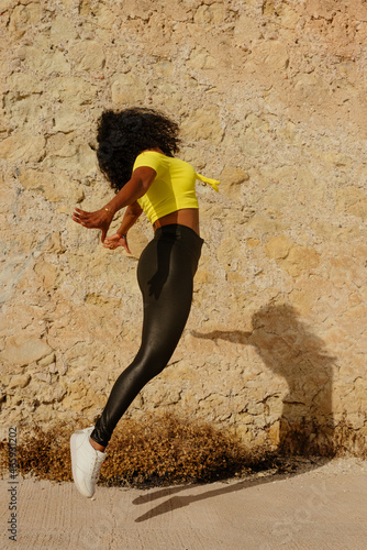 Latin black girl jumps for joy outdoors, yellow wall background