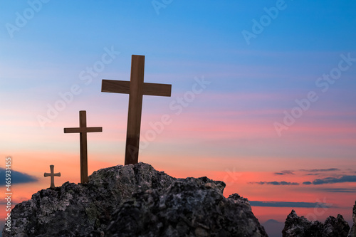 Silhouettes of crucifix symbol on top rock mountain with bright sunbeam on the colorful sky background