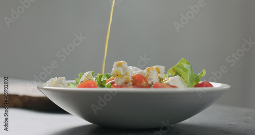 add olive oil to salad with cherry tomatoes and ricotta in white bowl