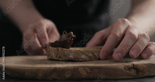 man spreading chocolate hazelnut spread on ciabatta slice on wood board