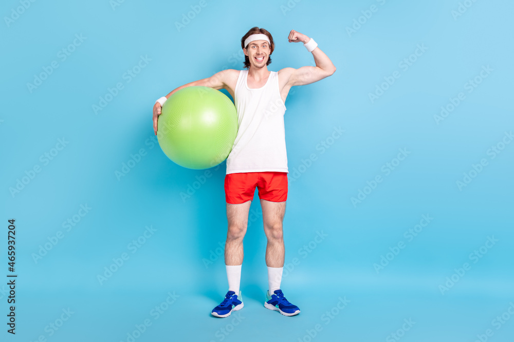 Full length body size photo strong man keeping fit ball showing biceps isolated pastel blue color background Full length body size photo strong man keeping fit ball showing biceps isolated pastel blue color background