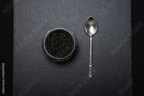 black sturgeon caviar in a glass jar and a silver teaspoon on a slate plate - flatley