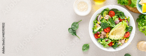 Avocado and tuna fresh vegetable salad with tomato, cucumber corn, onion, lettuce and spinach. Healthy and detox food concept. Ketogenic diet. Buddha bowl dish on light background. Top view. Banner.