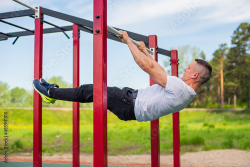 Caucasian man doing a back plank on the uneven bars. Workout on the sports ground.