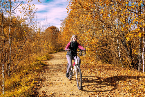 A girl rides a recreational bicycle through the park. Autumn leaves fall. A sunny autumn day.