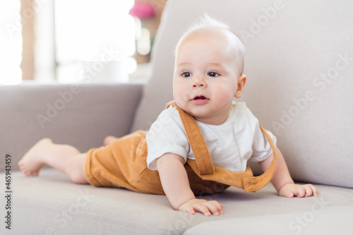 Photo of curious cute small kid baby boy lay comfortable sofa look away wear suspenders home indoors