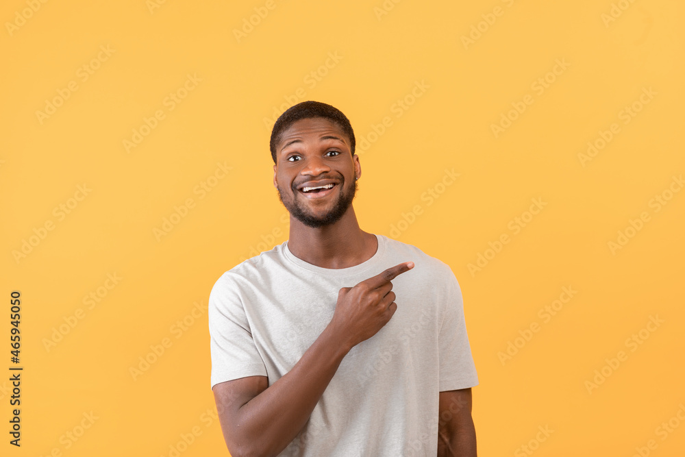 Look aside. Surprised black man pointing finger and showing copy space for advertisement text, yellow background Look aside. Surprised black man pointing finger and showing copy space for advertisement text, yellow background