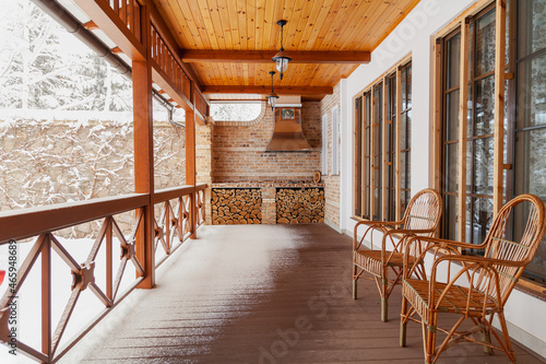 Two wicker chairs stand on veranda on winter day