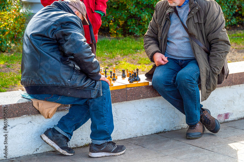 Two elderly retired men play chess outdoors on a city street. Leisure for people of retirement age.