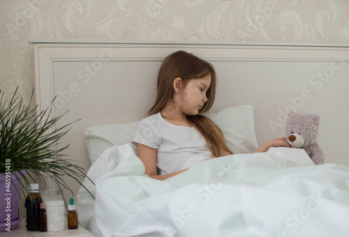 Schilderij op canvas A sick child is sick at home, lying in bed with a teddy bear and burying medicine in his nose
