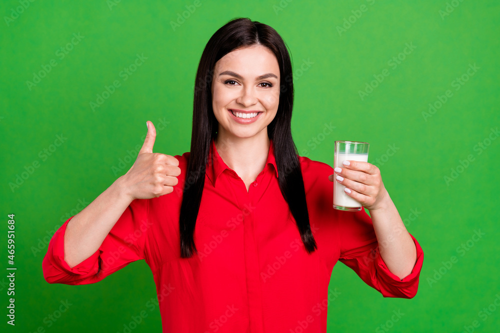 Photo of cool brunette young lady drink milk show thumb up wear red shirt isolated on green color background Photo of cool brunette young lady drink milk show thumb up wear red shirt isolated on green color background