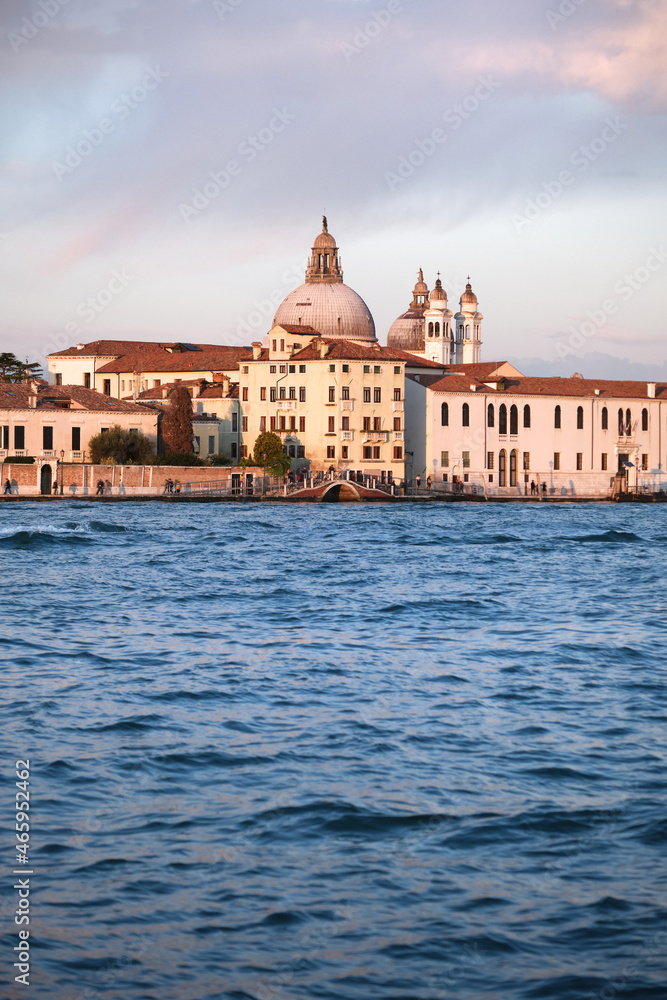 Old buildings on Dorsodouro promenade and cupola of Santa Maria della Salute church in Venice, Italy. Traditional Venetian architecture. Vertical image with sea water in front.