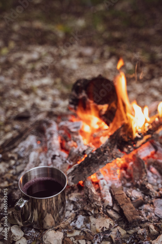 A metal mug with a drink stands next to the fire. Picnic in a camp in the woods. Fireplace in the camp, twilight