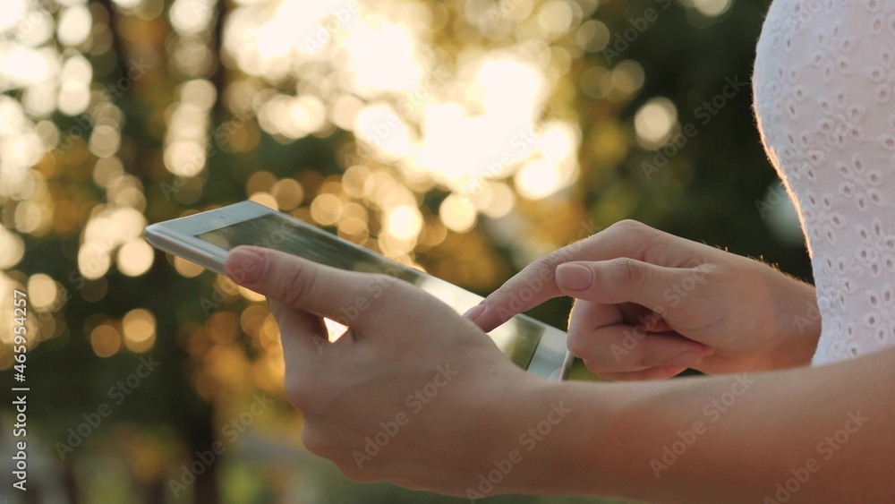 A young girl holds in her hand a modern tablet in the glare of the sunset, go online to the Internet, the rays of the sun shine on the touch screen of the tablet, the concept of modern technologies