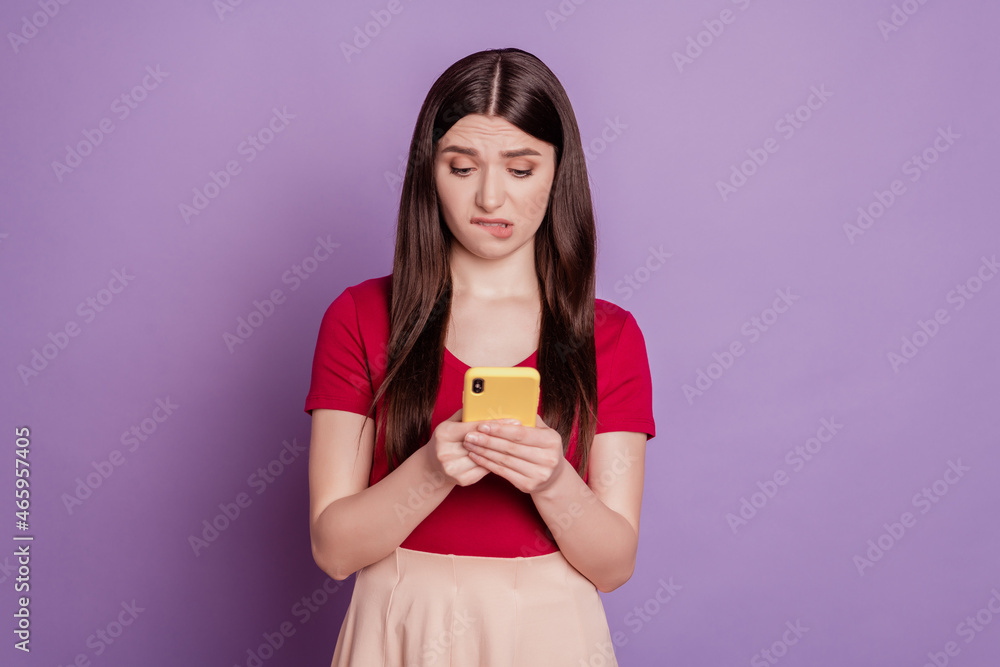 Portrait of guilty sorry girlish lady hold phone look screen bite lip on violet background Portrait of guilty sorry girlish lady hold phone look screen bite lip on violet background